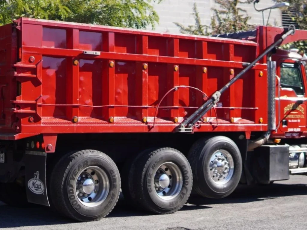 A red tri-axle Mack dump truck from Bombace Construction parked on site, used for hauling demolition debris in New Rochelle, NY.