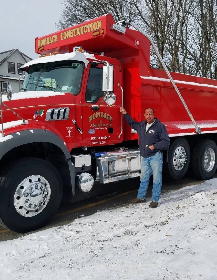 John Bombace, owner of Bombace Construction standing in front of a red tri axle Mack dump truck that is available for rent with a licensed operator